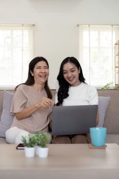 Senior mother and adult daughter relaxing and looking at laptop together at home.