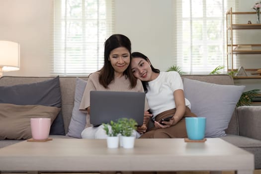 Senior mother and adult daughter relaxing and looking at laptop together at home.