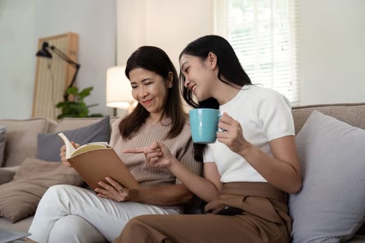 Happy senior mother with adult daughter sitting on couch and holding cups with coffee or tea at home. Enjoy family concept.