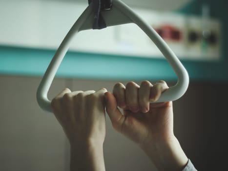 Caucasian male patient holds with both hands a triangular therapeutic archwire with a gripper set above the bed in a hospital room, close-up side view. The concept of trauma devices.