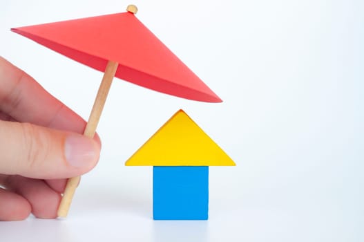 House shape toy covered with red umbrella representing house or property insurance concept.