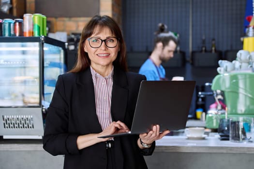 Portrait of confident business woman accountant financier lawyer small business owner. Successful middle-aged female using laptop computer looking at camera background coffee shop cafeteria restaurant