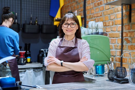 Portrait of 40s female small business owner entrepreneur in apron with crossed arms standing behind bar counter in coffee shop cafeteria cafe. Staff teamwork work service retail management success