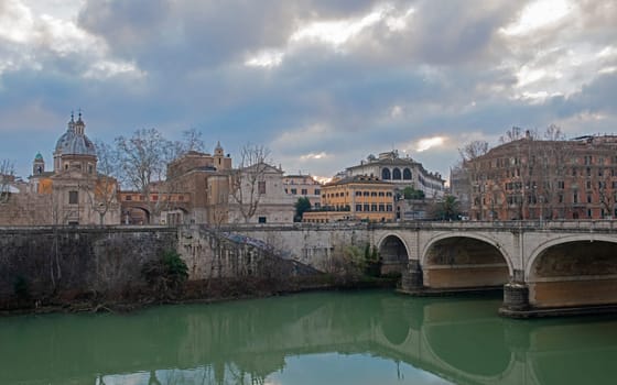Old stone arched road bridge over large river Tiber in Rome Europen city centre with overcast cloudy sky