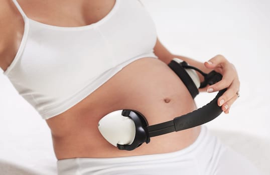 Woman, pregnant and headphones on stomach with music in studio for calming, parent or listening. Mother, audio and belly for soothing baby in womb for maternity bonding in home, streaming or relax.