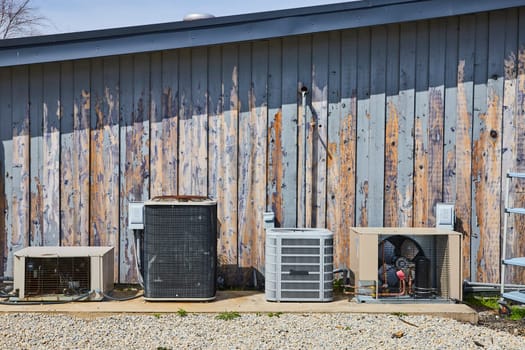 Quartet of air conditioning units aging gracefully on a rustic barnwood wall in Spiceland, Indiana, symbolizing utility and resilience.