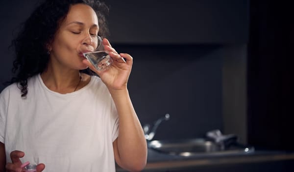 Close-up portrait of a young pretty woman drinking water in the morning, starting her day with a glass of refreshing water. Healthy lifestyle. Morning routine. People