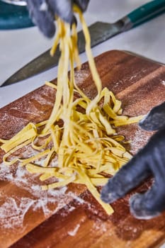Artisanal pasta making in Fort Wayne, Indiana. Skilled hands in black gloves separate fresh fettuccine on a rustic cutting board.