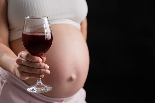 Close-up of the belly of a pregnant woman holding a glass of red wine while sitting on the sofa