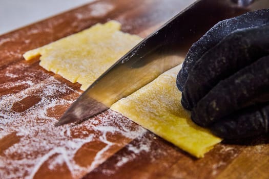 Artisanal pasta preparation in a rustic kitchen in Fort Wayne, Indiana, featuring a gloved hand delicately slicing fresh tagliolini dough.