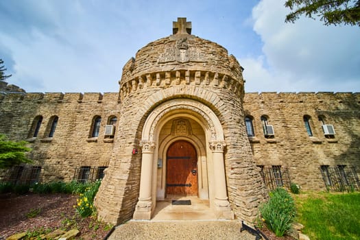 Bishop Simon Brute College medieval-style stone tower under partly cloudy Indiana sky, featuring a cross and ornate wooden door.