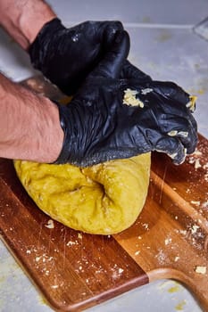 Artisanal pasta making in Fort Wayne, Indiana - gloved hands expertly kneading fresh, yellow dough on a rustic wooden board.