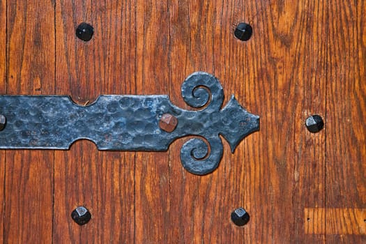 Artisanal wrought iron hinge on an antique wooden door at Bishop Simon Brute College, symbolizing timeless craftsmanship.