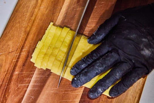 Safe culinary practices in a kitchen in Fort Wayne, Indiana, featuring a fresh folded pasta sheet being precisely sliced on a well-used wooden board