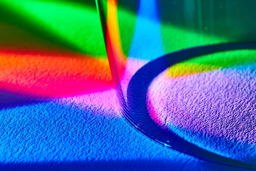 Abstract macro shot of light refracting through a wine glass creating a vibrant rainbow spectrum on textured surface, demonstrating color theory