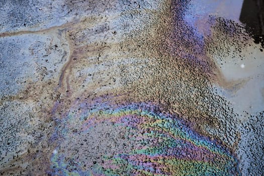 Abstract colored background of leaked gasoline on wet asphalt close-up.