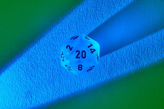 Luminous blue twenty-sided die casting shadow on contrasting green and blue backdrop, symbolizing gaming strategy and the thrill of chance.