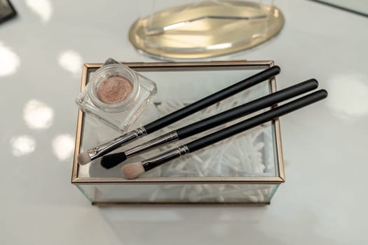 A small box with three makeup brushes and a jar of powder
