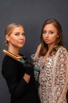 Two women are posing for a photo, one holding a hair curler. Scene is casual and friendly, as the women are smiling and looking at the camera