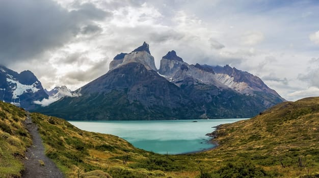 Sweeping view of grand mountains beside a vibrant turquoise lake under a cloudy sky.