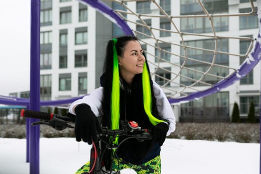 A woman is sitting on a bike, parked in front of a basketball hoop. She appears to be taking a break or enjoying the view.