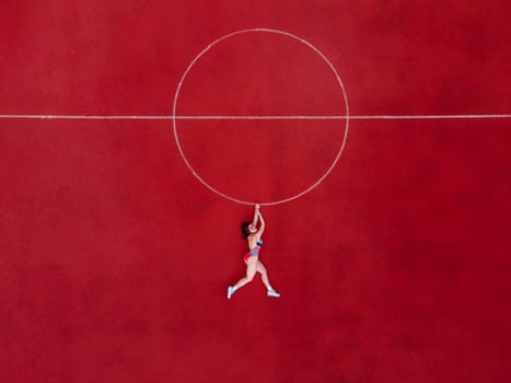 Abstract aerial shot of woman in swimwear hanging holding a circle on basketball field. SWAG concept