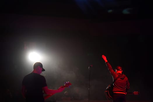 Rock band vocalist silhouette with the guitar singing to microphone with the hands raised up in red lights on the concert