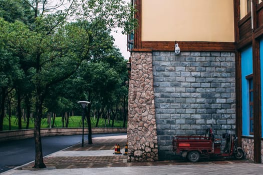 Brick wall of building in chinese park. Asphalt road, motorbike, trees. China, Anhui province