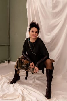 A woman is sitting on a chair with her legs crossed and wearing a black dress. She is holding a handbag and has a necklace around her neck. Concept of elegance and sophistication