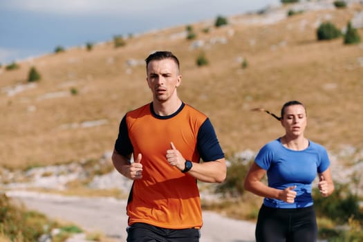 A couple dressed in sportswear runs along a scenic road during an early morning workout, enjoying the fresh air and maintaining a healthy lifestyle.