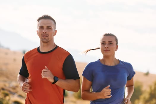 A couple dressed in sportswear runs along a scenic road during an early morning workout, enjoying the fresh air and maintaining a healthy lifestyle.