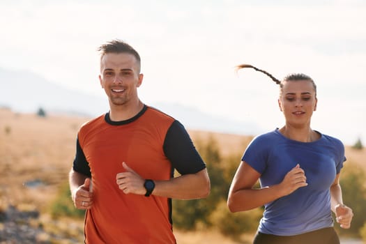 A couple dressed in sportswear runs along a scenic road during an early morning workout, enjoying the fresh air and maintaining a healthy lifestyle.