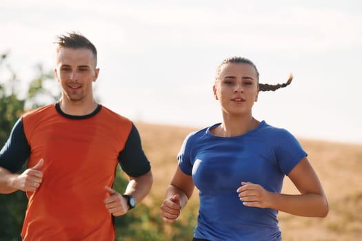 A couple dressed in sportswear runs along a scenic road during an early morning workout, enjoying the fresh air and maintaining a healthy lifestyle.