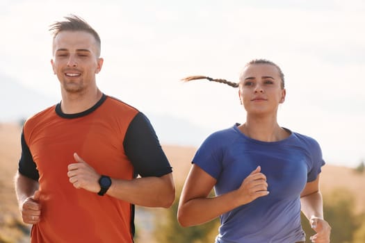 A couple dressed in sportswear runs along a scenic road during an early morning workout, enjoying the fresh air and maintaining a healthy lifestyle.