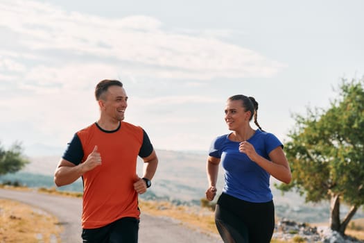 A couple dressed in sportswear runs along a scenic road during an early morning workout, enjoying the fresh air and maintaining a healthy lifestyle.