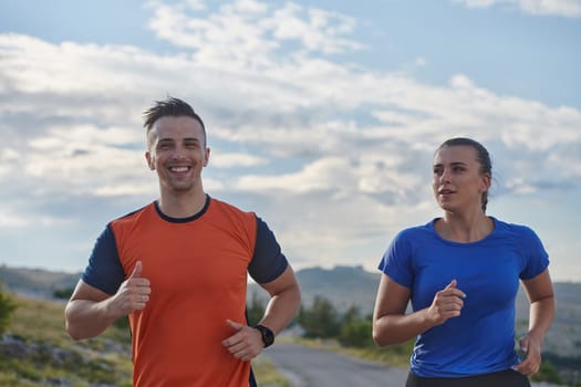 A couple dressed in sportswear runs along a scenic road during an early morning workout, enjoying the fresh air and maintaining a healthy lifestyle.