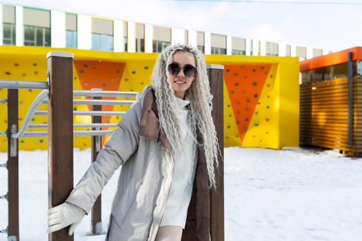 A woman is standing next to a wooden fence in a snowy landscape. She is wearing winter clothing and appears to be observing her surroundings.