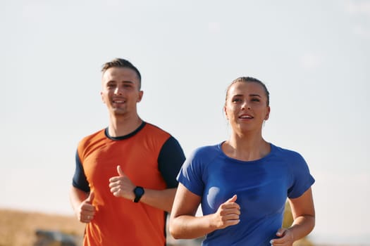 A couple dressed in sportswear runs along a scenic road during an early morning workout, enjoying the fresh air and maintaining a healthy lifestyle.