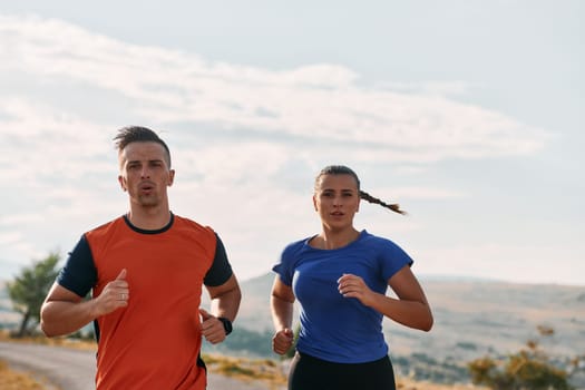 A couple dressed in sportswear runs along a scenic road during an early morning workout, enjoying the fresh air and maintaining a healthy lifestyle.