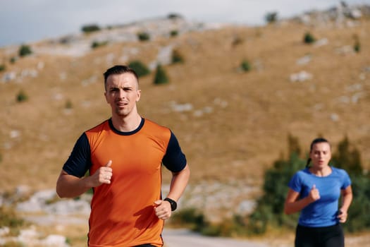 A couple dressed in sportswear runs along a scenic road during an early morning workout, enjoying the fresh air and maintaining a healthy lifestyle.