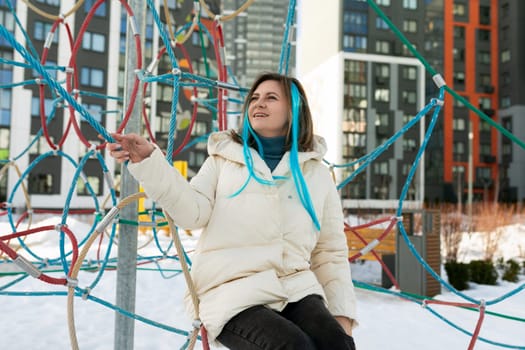 A woman sits atop a tall, sturdy metal pole. She appears balanced and comfortable in her precarious position, her gaze focused below. The surroundings suggest an urban environment.