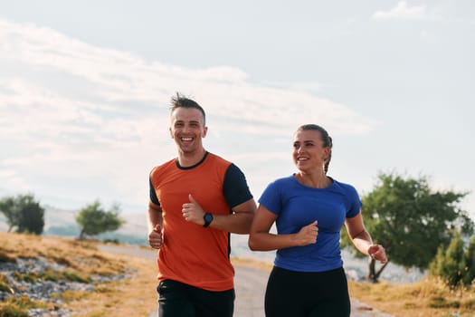 A couple dressed in sportswear runs along a scenic road during an early morning workout, enjoying the fresh air and maintaining a healthy lifestyle.