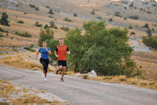 A couple dressed in sportswear runs along a scenic road during an early morning workout, enjoying the fresh air and maintaining a healthy lifestyle.