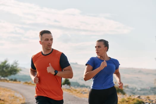 A couple dressed in sportswear runs along a scenic road during an early morning workout, enjoying the fresh air and maintaining a healthy lifestyle.