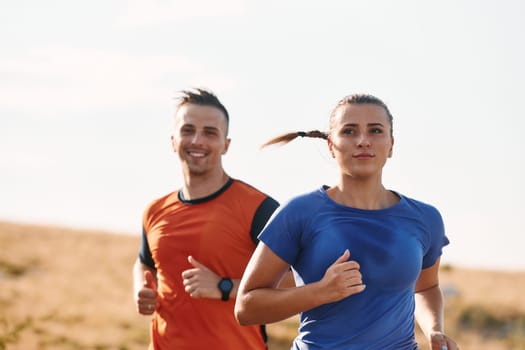 A couple dressed in sportswear runs along a scenic road during an early morning workout, enjoying the fresh air and maintaining a healthy lifestyle.