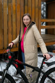 A woman is standing next to a bicycle in a snowy winter scene. She appears to be preparing to ride the bike despite the cold weather.