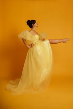 A woman in a yellow dress is posing for a photo. The dress is long and has a polka dot pattern. The woman is standing on one leg, and the photo is taken on a yellow background