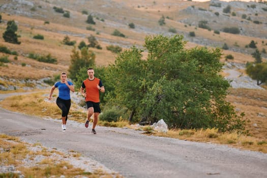 A couple dressed in sportswear runs along a scenic road during an early morning workout, enjoying the fresh air and maintaining a healthy lifestyle.