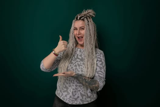 A woman with dreadlocks is smiling and giving a thumbs up gesture. Her dreadlocks are styled in a neat and tidy manner. She appears confident and positive in her expression.