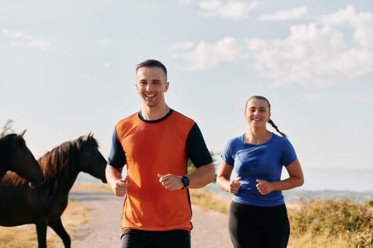 A couple dressed in sportswear runs along a scenic road during an early morning workout, enjoying the fresh air and maintaining a healthy lifestyle.